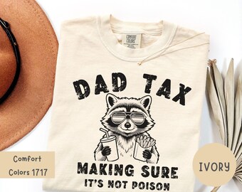 Puede incluir: Camiseta de color marfil con el texto "DAD TAX" sobre un mapache con gafas de sol que sostiene una bebida y patatas fritas. El texto "MAKING SURE IT'S NOT POISON" está debajo. La camiseta es Comfort Colors 1717.