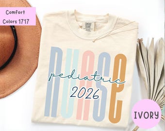 Puede incluir: Una camiseta de color marfil con la palabra NURSE en letras mayúsculas verticales y multicolores en tonos azul, verde azulado, rosa y naranja. La palabra pediatric está escrita en cursiva verde azulado oscuro en el centro, con 2026 debajo.