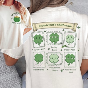 May include: Cream-colored t-shirt with a St. Patrick's Day theme. The front features a green pot of gold and the text "St Patrick shift scale." The back displays a chart with shamrock illustrations and phrases like "Green Alert" and "Pot o' Trouble Blast."