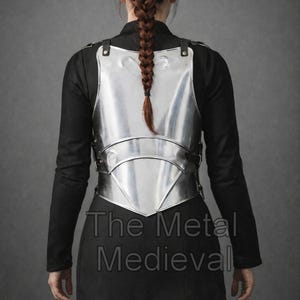 May include: A polished silver metal breastplate with leather straps, worn over a black garment. The text "The Metal Medieval" is visible on the lower portion of the image. The breastplate is a historical garment.