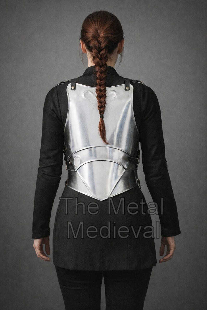 May include: A polished silver metal breastplate with leather straps, worn over a black garment. The text "The Metal Medieval" is visible on the lower portion of the image. The breastplate is a historical garment.