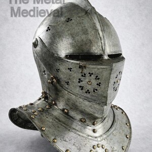 May include: A detailed, close-up view of a medieval steel helmet. The helmet features a visor with decorative cutouts and is adorned with rivets. The text "The Metal Medieval" is visible in the upper left corner. The helmet is a silver-gray color.