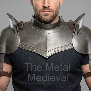 May include: A steel-colored medieval shoulder armor set with a neck guard and shoulder plates. The armor is riveted and has leather straps. The text "The Metal Medieval" is visible on the dark blue shirt.