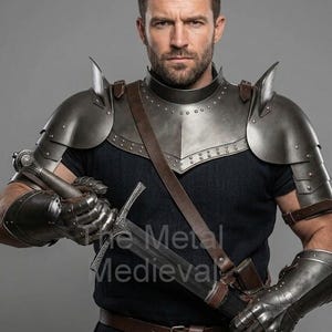 Può includere: Una persona indossa un'armatura medievale color argento, tra cui spallacci, protezioni per le braccia e gorgiera. L'armatura è rivettata. Una spada è tenuta nella mano destra. Il logo The Metal Medieval è visibile.