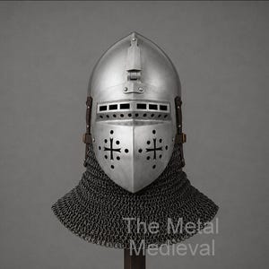 May include: A silver-colored medieval helmet with a visor featuring cross-shaped cutouts. The helmet has a riveted construction and is paired with a chainmail neck guard. The Metal Medieval is printed at the bottom.