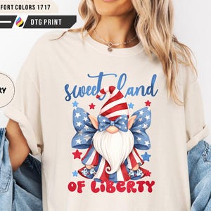 Könnte beinhalten: Cremefarbenes T-Shirt mit einem patriotischen Zwerg-Design. Der Zwerg trägt einen rot-weiß-blauen Hut und eine Fliege mit den Worten "sweet land of liberty" in Blau und Rot.