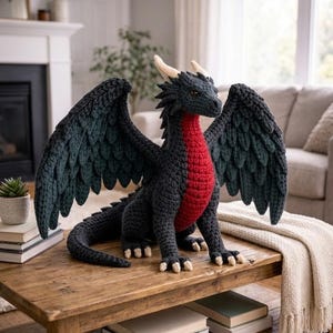 Puede incluir: Un dragón de ganchillo hecho a mano, predominantemente negro con un pecho rojo y cuernos crema. Las alas están extendidas. El dragón se exhibe sobre una mesa de madera. Es un objeto decorativo.
