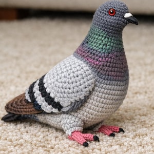 May include: A handmade crochet pigeon in shades of gray, blue, green, and pink. The bird has red eyes, a black beak, and pink feet with black claws. The wings feature black and white stripes. A unique, handcrafted decorative item.