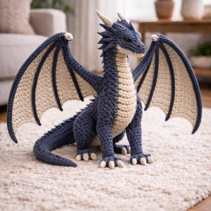 Puede incluir: Un dragón de ganchillo hecho a mano en tonos azules y beige. La criatura mítica tiene alas extendidas, cuernos y escamas detalladas. El dragón está sentado sobre una alfombra color crema, mostrando el intrincado trabajo de ganchillo.