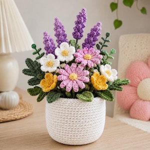 Può includere: Una composizione floreale all'uncinetto fatta a mano in un vaso bianco. Il bouquet presenta lavanda viola, margherite bianche e rosa e fiori gialli con foglie verdi. Il vaso è fatto di filo bianco.