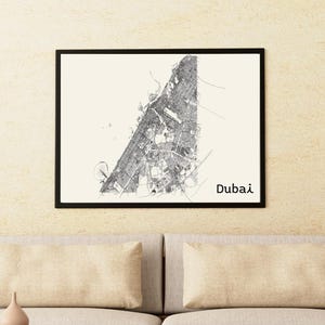 May include: A framed black and white map of Dubai, with the city's name printed in a simple font. The map is displayed on a light-colored wall above a modern sofa with beige cushions and a wooden coffee table.