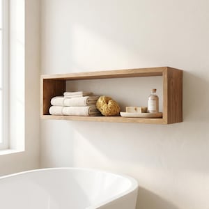 May include: A rectangular wooden wall shelf featuring a natural grain finish. Inside the shelf, there is a stack of folded beige towels, a textured natural sea sponge, a small clear glass bottle with a cork stopper, and a bar of soap on a tray.