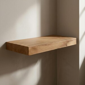 May include: A rectangular, floating wooden shelf. The shelf is made of light-colored wood and is mounted on a neutral-colored wall. The shelf is approximately 30 inches long and 10 inches wide, with a thick, solid appearance. The wood grain is visible.