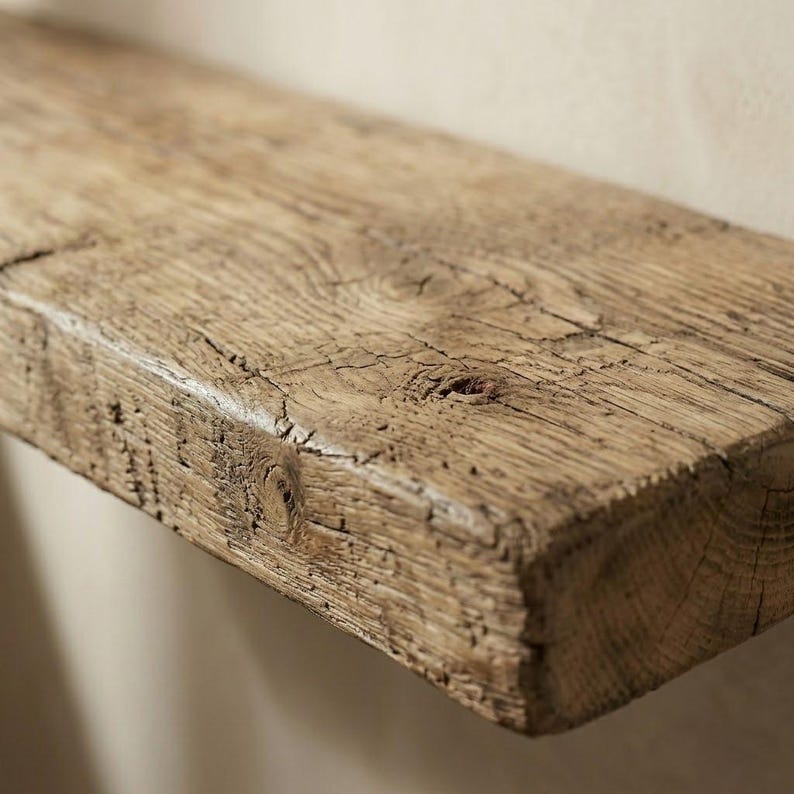 Pu&ograve; includere: Primo piano di una mensola in legno rustico. La mensola &egrave; realizzata in legno marrone chiaro, invecchiato, con venature, nodi e crepe visibili, che le conferiscono un aspetto naturale e invecchiato. La mensola &egrave; montata su una parete di colore neutro.