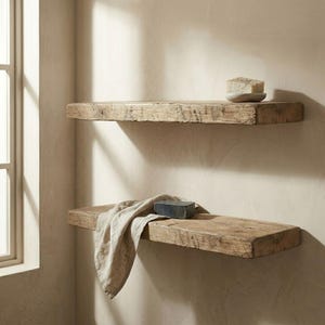Pu&ograve; includere: Due mensole in legno rustico montate su una parete beige. La mensola superiore contiene un piccolo sapone chiaro su un piatto rotondo. La mensola inferiore ha un panno beige piegato e una saponetta grigio scuro. Le mensole sono in legno stagionato.