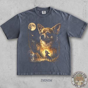 Pu&ograve; includere: T-shirt color denim con un'illustrazione dettagliata di un Chihuahua, una luna piena e una scena di foresta. Un Chihuahua pi&ugrave; piccolo ulula alla luna. La parola "DENIM" &egrave; stampata in basso.