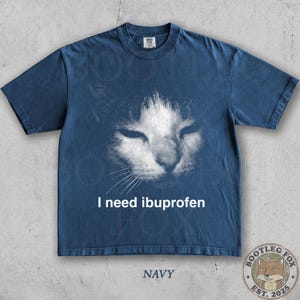 May include: Navy blue t-shirt featuring a distressed graphic of a cat's face with the text "I need ibuprofen". The shirt also has the word "NAVY" printed at the bottom and a logo of a fox.
