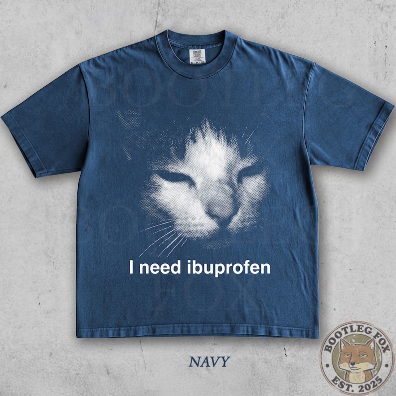 May include: Navy blue t-shirt featuring a distressed graphic of a cat's face with the text "I need ibuprofen". The shirt also has the word "NAVY" printed at the bottom and a logo of a fox.