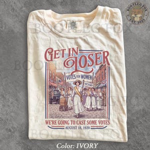 Könnte beinhalten: Ein elfenbeinfarbenes T-Shirt mit einem Grafikdruck einer historischen Szene, in der Menschen für das Wahlrecht demonstrieren. Der Text lautet: GET IN LOSER, VOTES FOR WOMEN, VICTORY, WE'RE GOING TO CAST SOME VOTES und AUGUST 18, 1920.