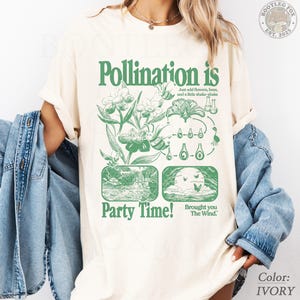 May include: An ivory t-shirt featuring a green graphic print with the text Pollination is Party Time! and Brought you The Wind. The design includes illustrations of flowers, bees, and a pollination cycle diagram with scientific laboratory glassware.