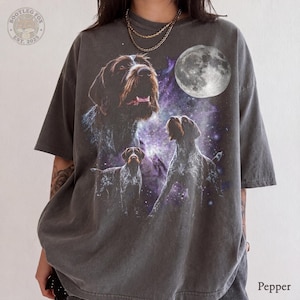 May include: A charcoal gray short-sleeve t-shirt featuring a graphic print of three wirehaired pointing griffon dogs against a purple nebula background with a full moon. The top left corner displays a circular logo with the text Bootleg Fox Est. 2025.