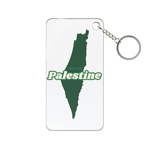 May include: A white rectangular keychain with a green outline of Palestine. The text "FREE FREE Palestine" is printed in green with a white outline. A silver-colored chain and keyring are attached.