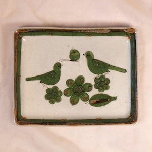 May include: Rectangular ceramic tray with a white background and a green border. The tray features green birds, flowers, and a butterfly design. The tray's border has a brown and green trim.