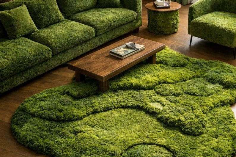 May include: A living room set with a moss-like theme. The set includes a green sofa, armchair, and a round side table. A wooden coffee table sits on a large, green, textured rug. The room has a natural, organic aesthetic.