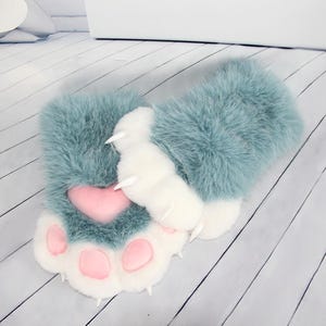 Puede incluir: Un par de guantes sin dedos de felpa diseñados para parecer patas de animal. Los guantes cuentan con piel sintética larga de color azul polvoriento, almohadillas de piel sintética blanca, almohadillas rosas en forma de corazón y garras.
