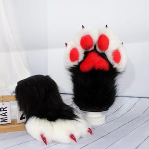 Può includere: Guanti a forma di zampa pelosa in nero, bianco e rosso. I guanti hanno la pelliccia nera sul polso, bianca sulla zampa, cuscinetti rossi e artigli rossi. Il design è pensato per assomigliare a zampe di animali.