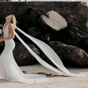 beach destination wedding with bride walking with head tilted back and two long cape shoulder wings blowing in the wind