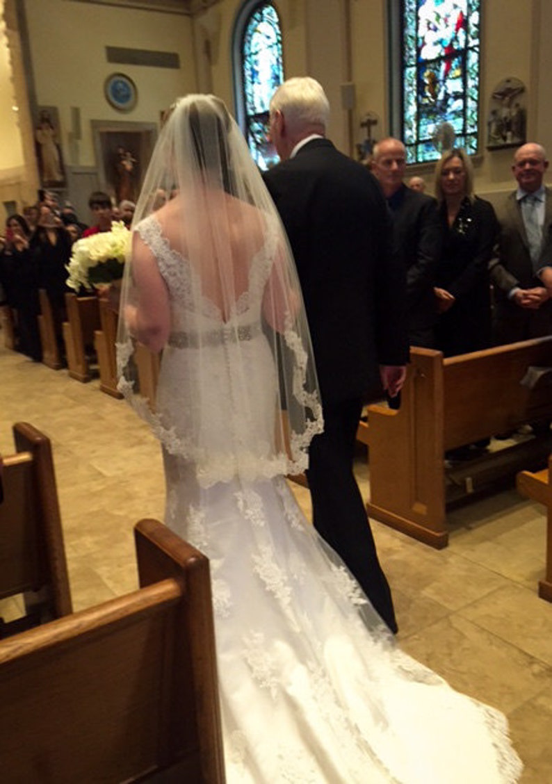 dad walking bride down the church aisle as bride wear lace V back dress and mid length lace edged fingertip wedding veil