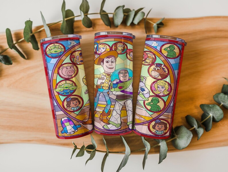 Puede incluir: Tres vasos de acero inoxidable con un colorido dise&ntilde;o de vidrieras que presenta personajes de una popular pel&iacute;cula de animaci&oacute;n. Los vasos tienen un borde y una base rojos, y una tapa transparente. El dise&ntilde;o incluye a Woody, Buzz Lightyear y otros personajes.