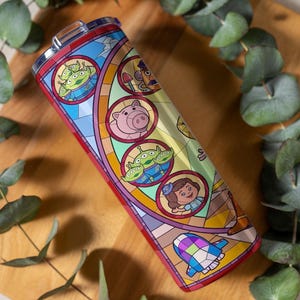 Puede incluir: Un vaso de acero inoxidable con un dise&ntilde;o de vidriera que presenta personajes de la pel&iacute;cula animada. El dise&ntilde;o incluye extraterrestres verdes, un cerdo rosa y otros personajes. El vaso mide aproximadamente 20 cm de alto.