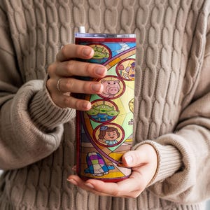 Puede incluir: Un vaso de acero inoxidable con un dise&ntilde;o de vidriera con personajes de dibujos animados. El vaso tiene una tapa transparente y una pajita. El dise&ntilde;o incluye im&aacute;genes de un cerdo, extraterrestres y una ni&ntilde;a.