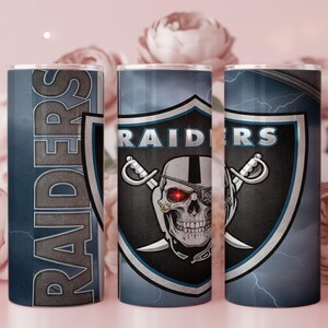 Könnte beinhalten: Drei Edelstahlbecher mit Raiders-Motiv. Das Design zeigt das Logo des Teams, einen Totenkopf mit Augenklappe und gekreuzten Schwertern, vor einem Schild. Das Wort "RAIDERS" ist vertikal auf einem Becher abgebildet.