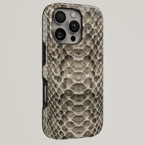 Puede incluir: Una funda para smartphone con un patrón detallado y texturizado de piel de serpiente en tonos beige, gris y marrón. La funda tiene un borde negro y un recorte para el sistema de triple cámara en la parte posterior del dispositivo.