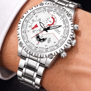 Op de afbeelding: Zilverkleurig chronograafhorloge met een witte wijzerplaat en rode accenten. Het horloge heeft meerdere sub-wijzerplaten, een datumweergave en een roestvrijstalen band. Het horloge wordt om de pols getoond.