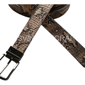 May include: A reversible belt with a snakeskin pattern in shades of brown and tan. The belt has a silver-colored buckle and the text "SVIN GRAP" is visible on the belt.