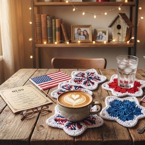 May include: A collection of star-shaped crochet coasters in red, white, and blue yarn. The coasters are arranged on a wooden table alongside a ceramic mug with latte art, a glass of water with ice, a small American flag, and a menu card.
