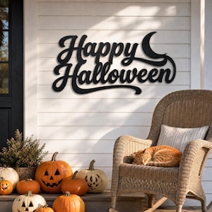 May include: A black metal wall sign featuring the text Happy Halloween in a cursive script with a crescent moon shape integrated into the design. The sign is mounted on a white horizontal paneled wall above a wicker rocking chair and pumpkins.