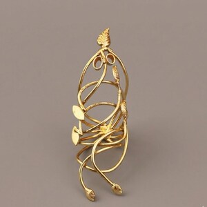 May include: A gold-colored, decorative ring with a leaf and swirl design. The ring features multiple spiraling bands and leaf-shaped accents. The ring is made of a shiny, metallic material and has a detailed, elegant appearance.