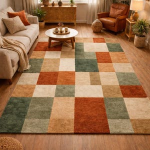Könnte beinhalten: Rechteckiger Teppich mit geometrischem Muster in Grün-, Beige-, Orange- und Brauntönen. Der Teppich liegt auf einem Holzboden in einem Wohnzimmer, mit Sofa, Sessel und Couchtisch im Hintergrund.