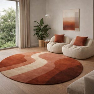 May include: A living room scene featuring a large, round rug with a wavy design in shades of rust, beige, and brown. Two cream-colored beanbag chairs with rust-colored pillows are visible, along with a sofa and a wooden bookshelf.