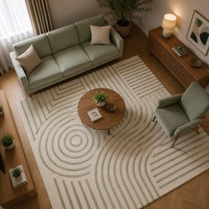 Könnte beinhalten: Ein großer rechteckiger Teppich mit cremefarbener Basis und erhabenen, salbeigrünen geometrischen Mustern aus konzentrischen Kreisen und parallelen Linien. Der Teppich liegt in einem Wohnzimmer mit Sofa, Sessel und einem runden Tisch.
