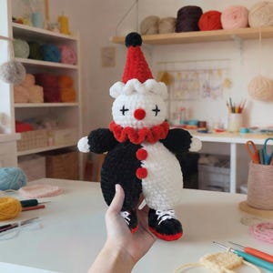 May include: A handmade plush clown doll in red and black. The clown has a red hat with a black pom-pom, a white ruffled collar, and a red nose. The doll's body is split between black and white, with black shoes and white laces.