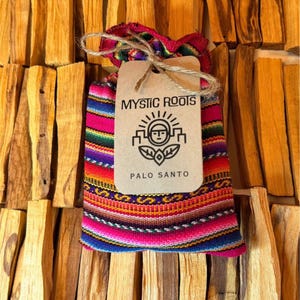 May include: A colorful bag of Palo Santo sticks with a tag that reads "Mystic Roots". The bag is made of woven fabric with a vibrant pattern of pink, blue, red, and yellow stripes. The background is filled with light brown Palo Santo sticks.