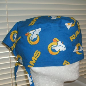 May include: Blue and yellow patterned surgical scrub hat with the word "RAMS" and a ram's head logo repeated throughout the fabric.