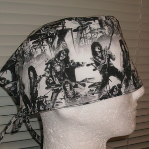 May include: Black and white patterned surgical scrub hat with a band of black fabric around the edge. The pattern features a band of musicians playing instruments and a crowd of people.