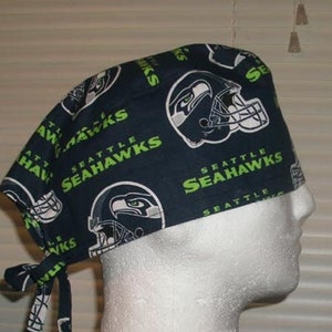 May include: A blue and green surgical scrub hat with a repeated pattern of the Seattle Seahawks logo. The logo features a football helmet with a green and white design.